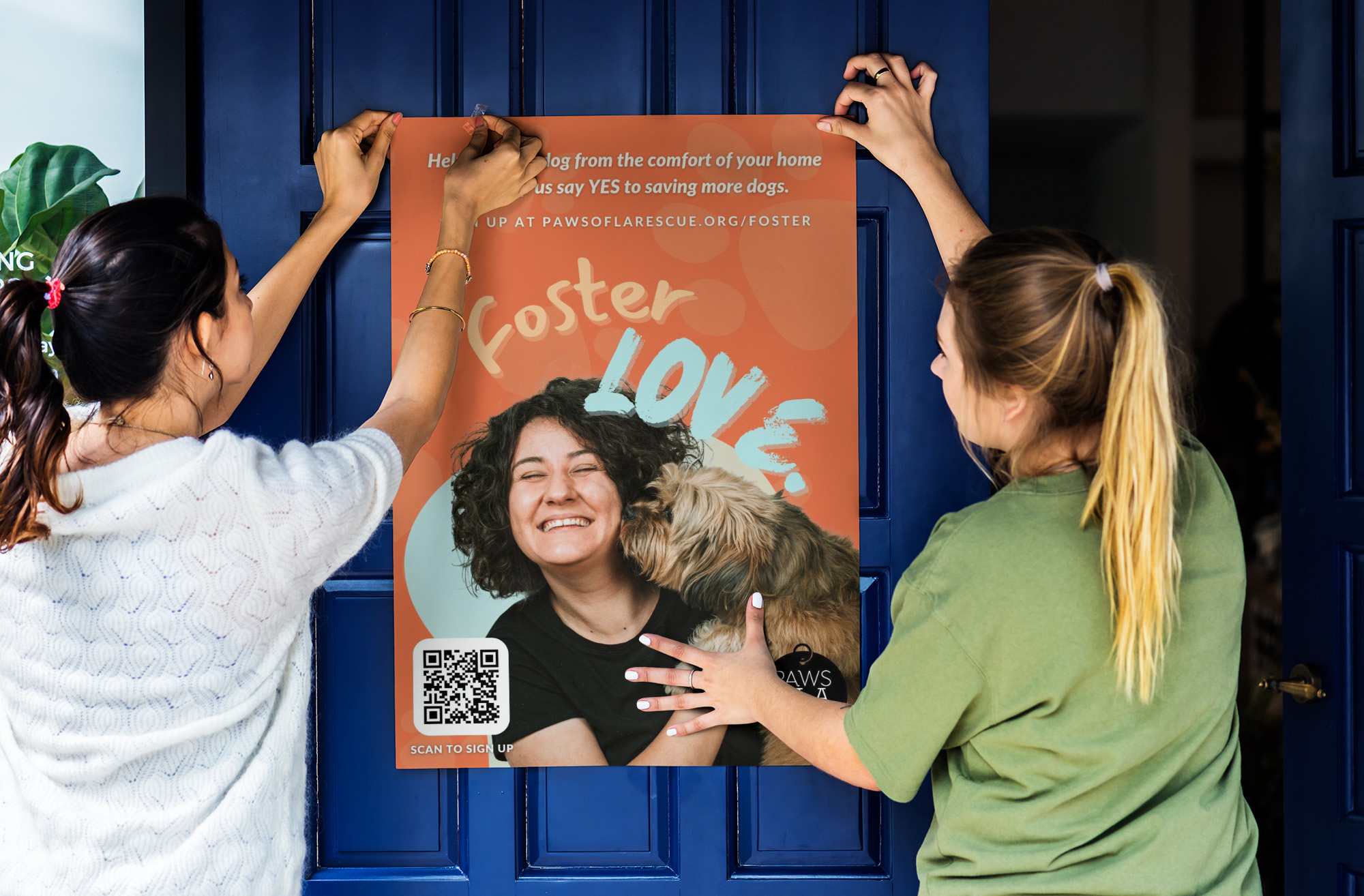 A mockup image of two people putting up a poster, which reads ‘Foster Love’ in cheerful orange and blue. The main image is a dog trying to lick a laughing person’s face.