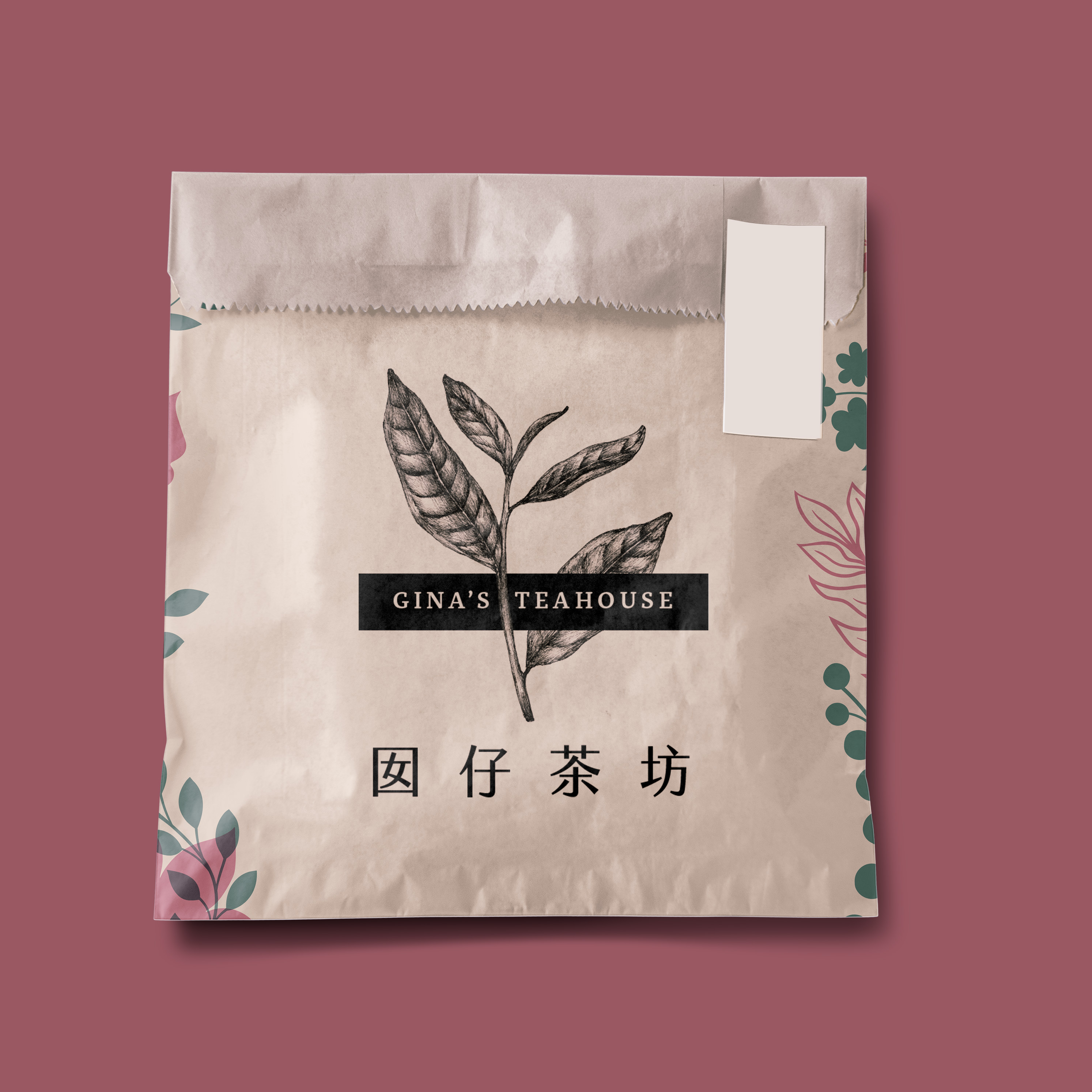 A mockup image of a light brown paper wrapping bag, such as for a cookie or pastry. On it is printed a logo reading 'Gina's Teahouse' in black with a vintage illustration of a tea leaf sprig. It is surrounded by green and pink floral illustrations.