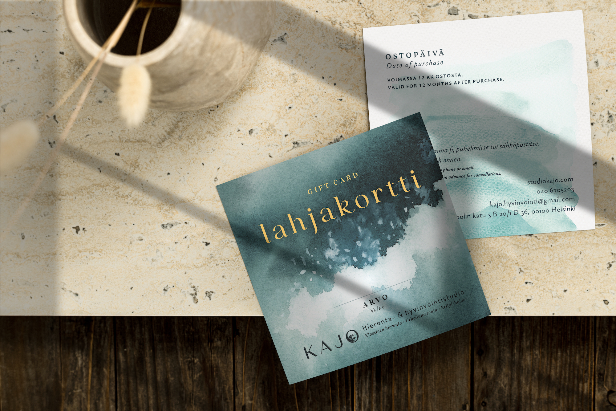 Mockups of the front and back of a large square gift certificate. The front has the 'Kajo' logo on a blue and white painted background of ocean waves. The reverse side is on a watercolor background of white and light aqua.