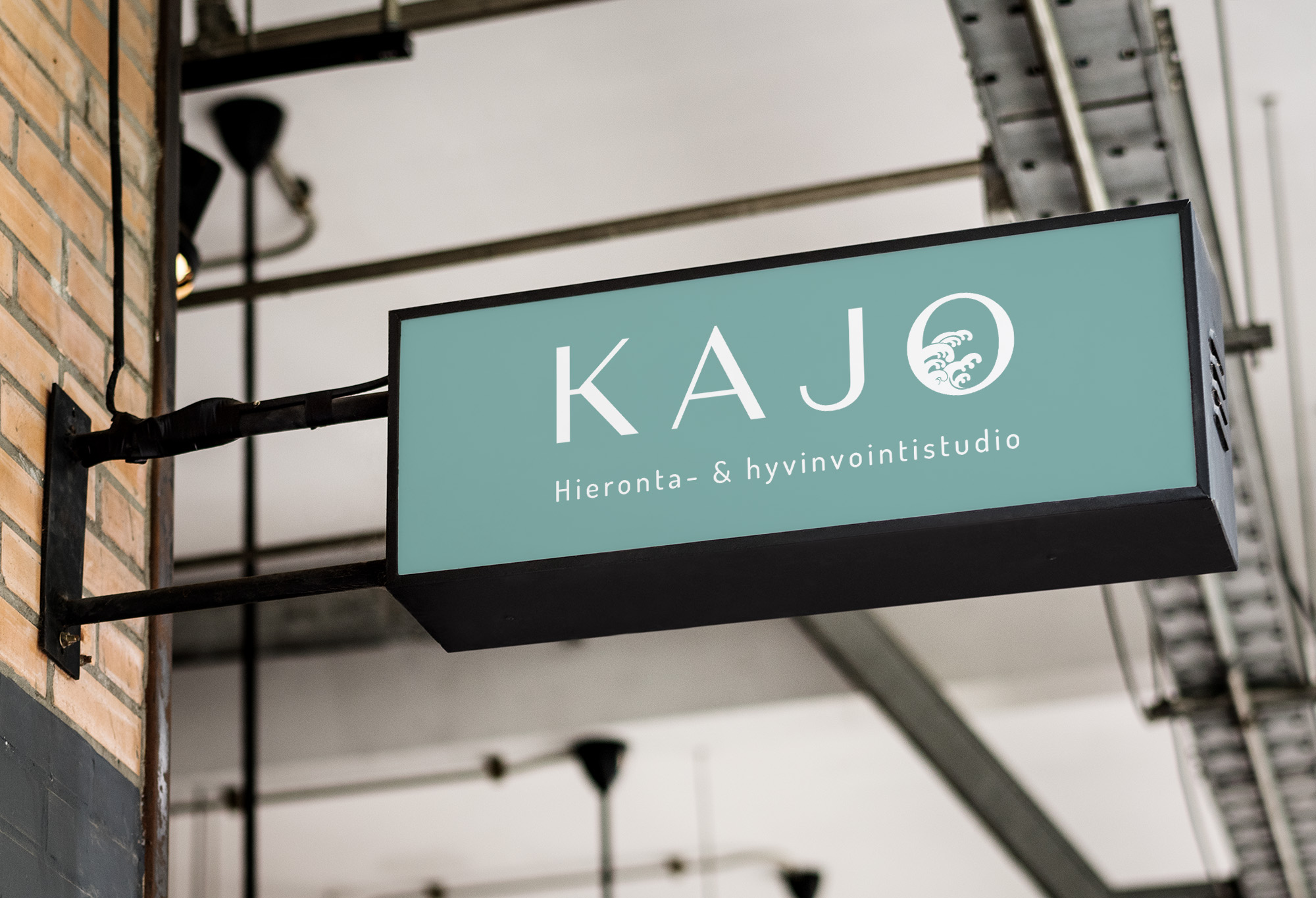 A mockup of the Kajo logo on a mounted signbox. It is printed in white on a seafoam green background.
